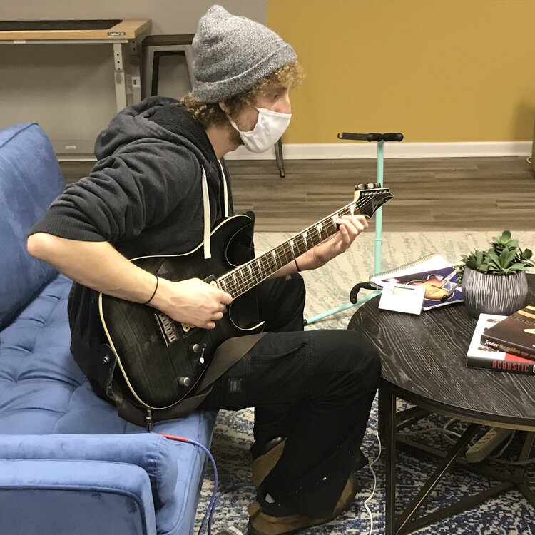 Instructor holding Guitar on couch at One Three Guitar